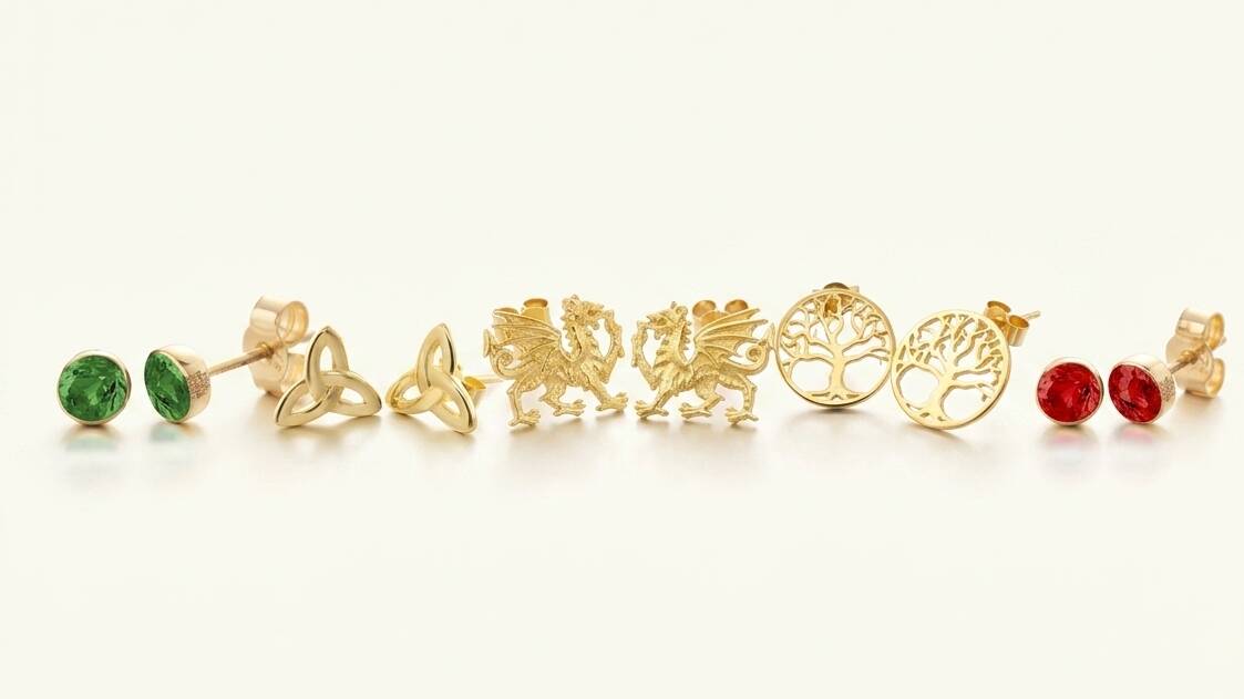 A wide-angle studio shot showcasing an array of Welsh gold stud earrings, including green gemstones, Celtic Trinity knots, Welsh dragons, filigree Trees of Life, and red rubies.