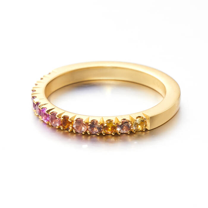A side-angle view of a flat-profile gold band set with a gradient of pink, orange, and yellow sapphires in a claw setting.